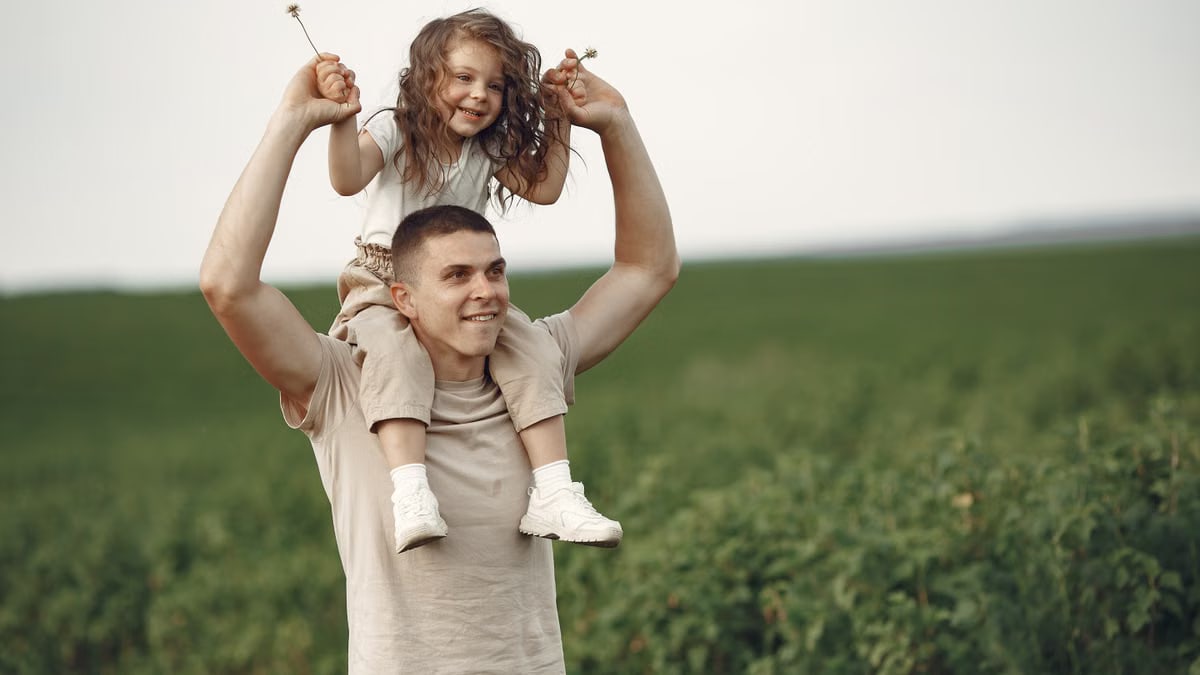 Happy father giving daughter a piggyback ride in a field, enjoying nature and family bonding.